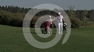 Happy man with his son golfers walking on perfect golf course at summer day