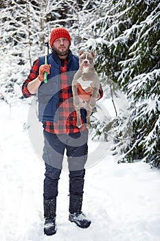 Happy man holding lovely dog in his hands in snowy forest. Smiling boy hugging adorable puppy in winter wood. Pet lover