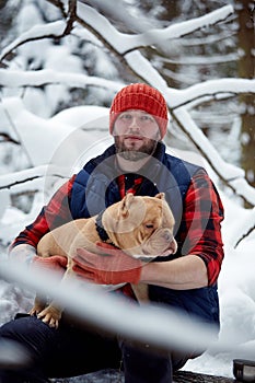 Happy man holding lovely dog in his hands in snowy forest. Smiling boy hugging adorable puppy in winter wood. Pet lover