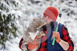 Happy man holding lovely dog in his hands in snowy forest. Smiling boy hugging adorable puppy in winter wood. Pet lover