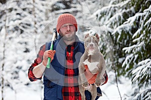 Happy man holding lovely dog in his hands in snowy forest. Smiling boy hugging adorable puppy in winter wood. Pet lover