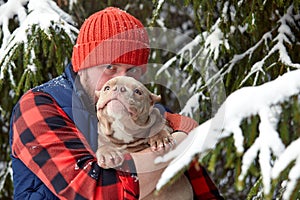 Happy man holding lovely dog in his hands in snowy forest. Smiling boy hugging adorable puppy in winter wood. Pet lover