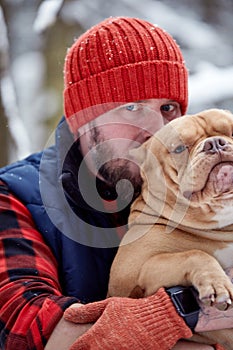 Happy man holding lovely dog in his hands in snowy forest. Smiling boy hugging adorable puppy in winter wood. Pet lover