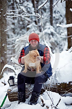 Happy man holding lovely dog in his hands in snowy forest. Smiling boy hugging adorable puppy in winter wood. Pet lover