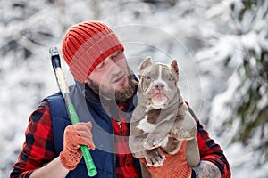 Happy man holding lovely dog in his hands in snowy forest. Smiling boy hugging adorable puppy in winter wood. Pet lover