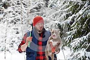 Happy man holding lovely dog in his hands in snowy forest. Smiling boy hugging adorable puppy in winter wood. Pet lover