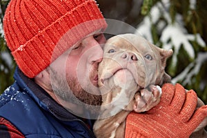 Happy man holding lovely dog in his hands in snowy forest. Smiling boy hugging adorable puppy in winter wood. Pet lover