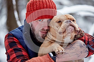 Happy man holding lovely dog in his hands in snowy forest. Smiling boy hugging adorable puppy in winter wood. Pet lover