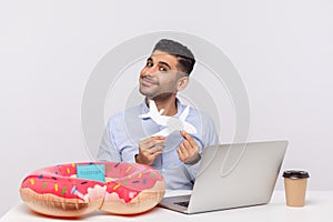 Happy man holding paper airplane smiling at camera, sitting in office workplace with rubber ring passport on desk