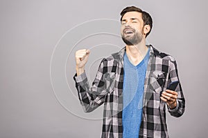 Happy man holding smartphone and celebrating his success isolated over grey background