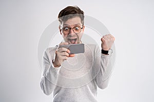 Happy man holding smartphone and celebrating his success over white background.