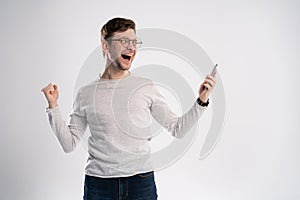 Happy man holding smartphone and celebrating his success over white background.