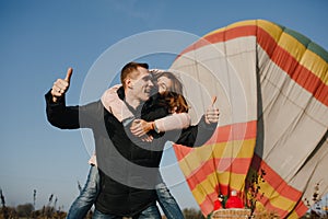 Happy man holding the smiling woman on his back and standing at the background of the balloon