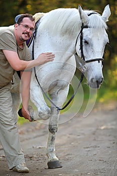 Happy man holds hoof of beautiful white horse in photo