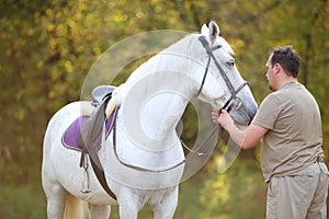 Happy man holds reins of beautiful white horse in photo