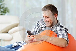 Happy man at home using mobile phone on a pouf