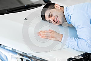 Happy Man Hugging New Car In Auto Dealership