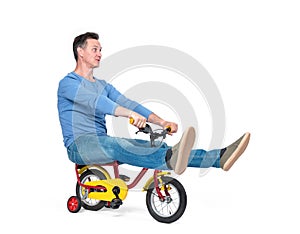 Happy man in jeans and t-shirt on a children`s bike, isolated on white background.