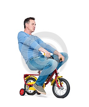 Happy man in jeans and t-shirt on a children`s bike, isolated on white background.