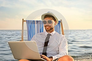 Happy man with laptop on deckchair near sea. Business trip