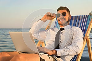 Happy man with laptop on deckchair near sea. Business trip