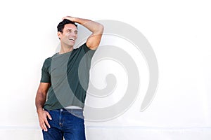 Happy man leaning against white wall and laughing with hand in hair