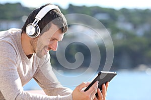 Happy man listening music with headphones on tablet on the beach