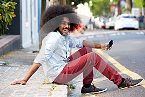 Happy man with mobile phone sitting on sidewalk