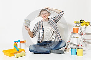 Happy man in newspaper hat holds bundle of dollars, cash money. Instruments for renovation apartment isolated on white