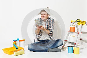 Happy man in newspaper hat holds bundle of dollars, cash money. Instruments for renovation apartment isolated on white