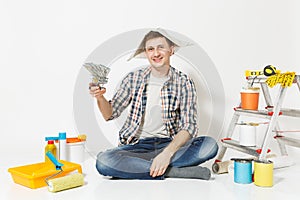 Happy man in newspaper hat holds bundle of dollars, cash money. Instruments for renovation apartment isolated on white