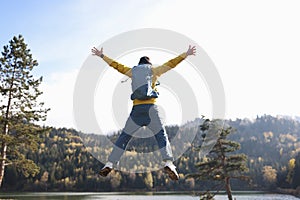 Happy man with open arms jumping, lake and mountains in background.