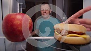 happy man opens the refrigerator and makes a choice between healthy and unhealthy food, apple or burger, unhealthy food