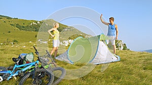 Happy man outstretches hand to high five girlfriend after setting up campsite.