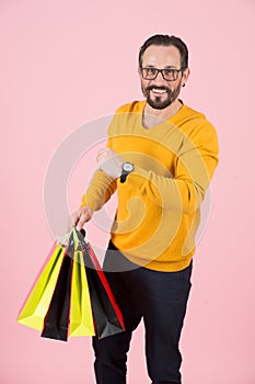 Bearded man has time for shopping. Smiling guy in glasses has time for new purchases. Happy man with paper bags showing time.