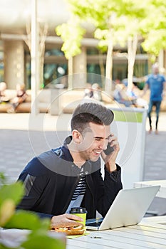 Happy man on phone call with laptop at cafe