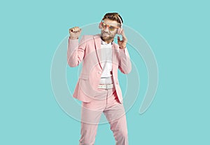 Happy man in pink suit and headphones listening music and dancing isolated on blue background.