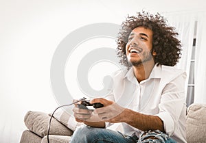 Happy man playing computer games. Young Arab guy entertains at home in self isolation during quarantine. Copy space at