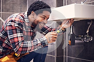 Happy, man or plumber fixing a sink with smile in maintenance or installation in home repairs. African handyman or
