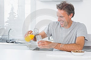 Happy man pouring orange juice for breakfast