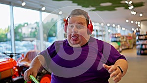 A happy man in a purple T-shirt and red headphones dances and walks along the counters in a large supermarket. Close-up