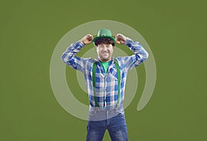 Happy man puts on a green hat and smiles standing isolated on a colour background