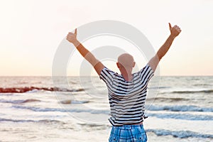 Happy man raises his arms up against the sea