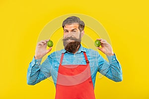 Happy man in red apron holding fresh limes citrus fruits yellow background, fruiterer photo