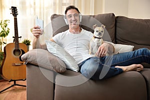 Happy man relaxing at home listening music with his dog