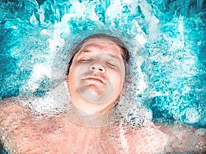Happy man relaxing in the jacuzzi and closing his eyes. Caucasian boy resting in a pool lies in water. View from above