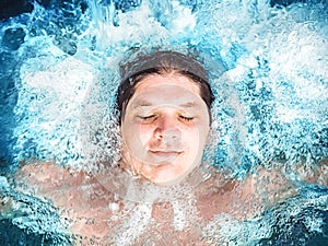 Happy man relaxing in the jacuzzi and closing his eyes. Caucasian boy resting in a pool lies in water. View from above