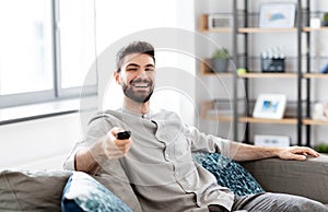 Happy man with remote control watching tv at home