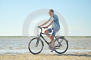 Happy man riding bicycle along summer beach