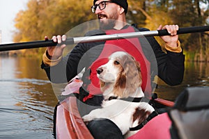 Happy man rowing a canoe with his spaniel dog, sunny autumn weather.
